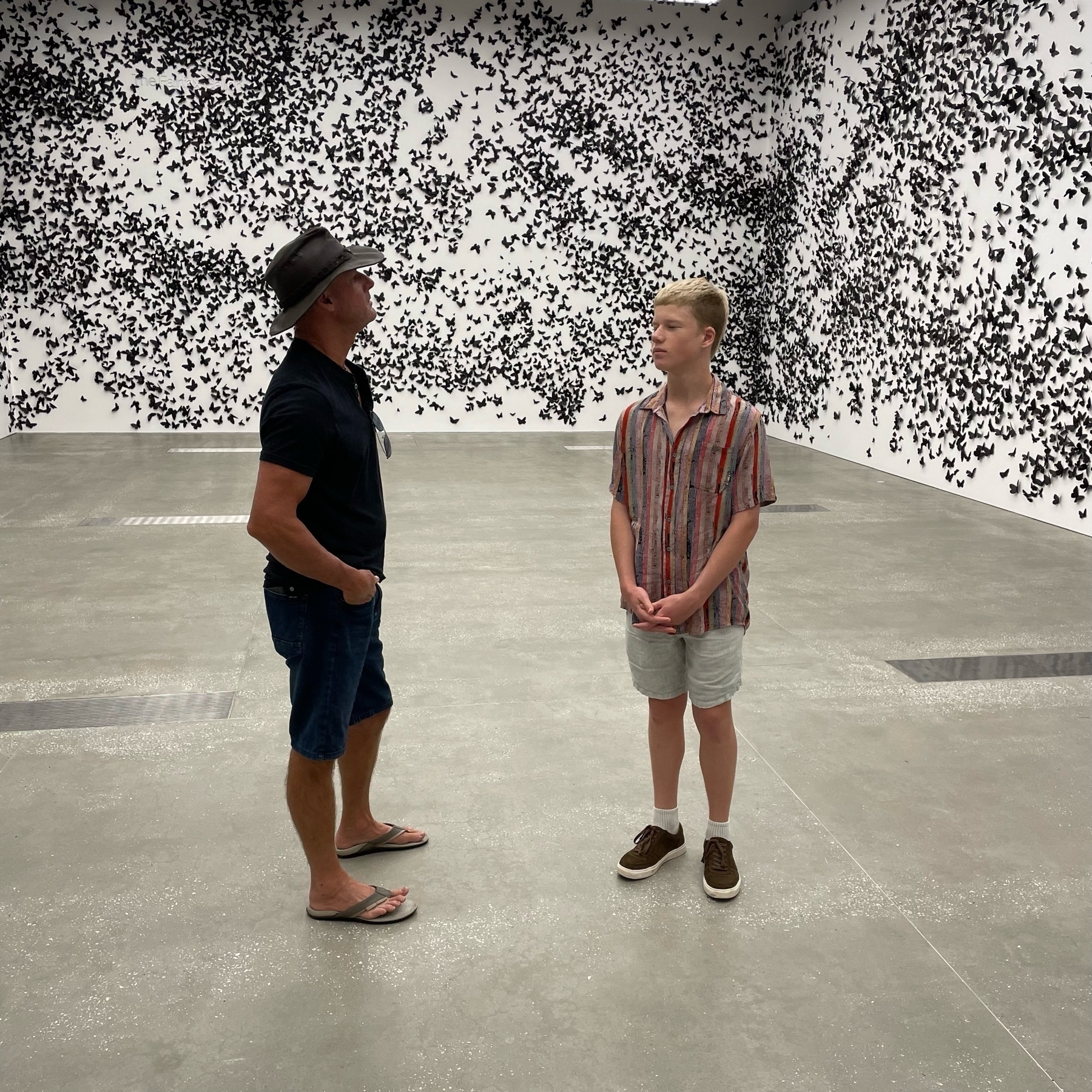 Two people standing in a room of thousands of black paper butterflies