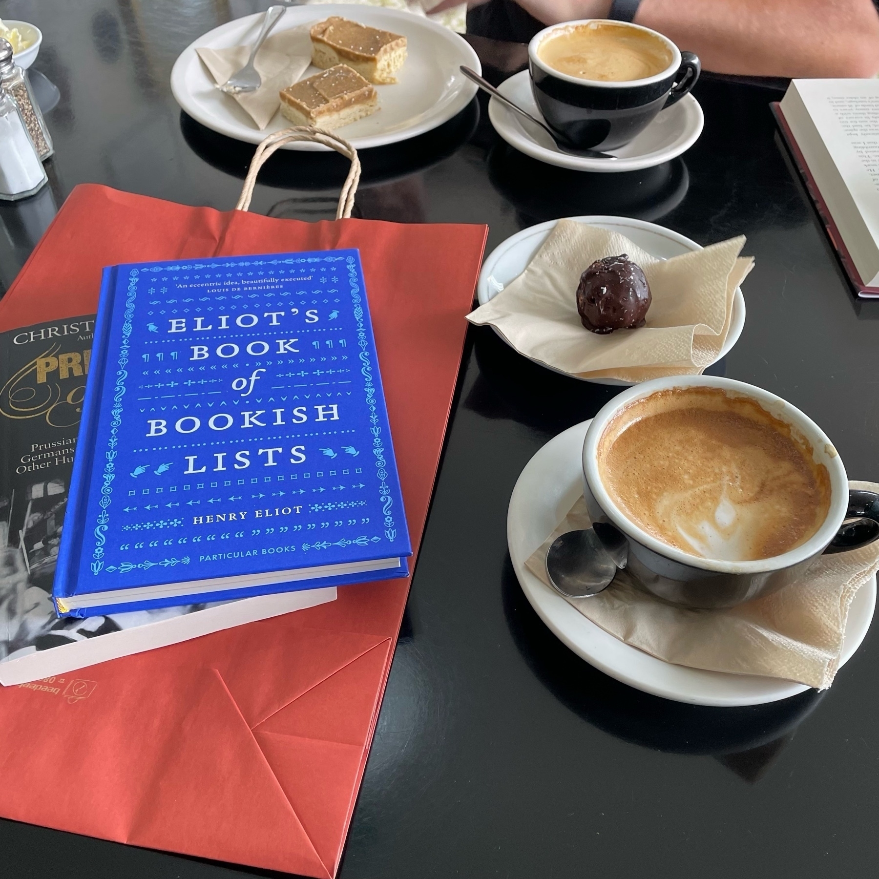 Two books (one titled “Eliot’s Book of Bookish List”) and two flat white coffees. 
